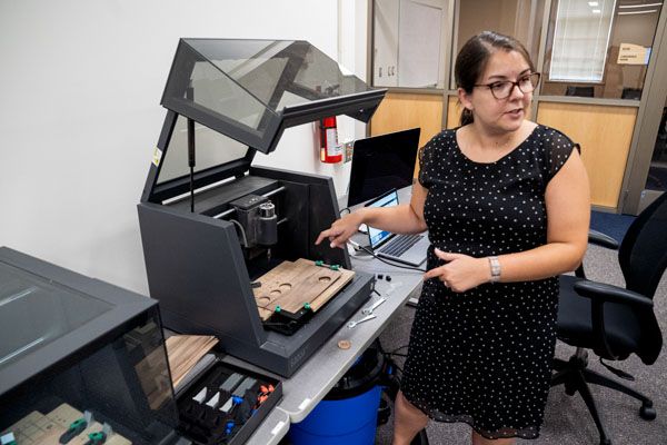Creation and innovation services librarian Sarah Nagle gestures at a Carvey CNC routing machine in the new Makerspace in King Library